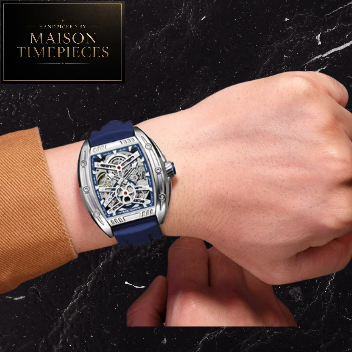 A close-up of a wrist wearing a Maison Timepieces skeleton watch with a blue strap and silver-tone case, shown against a dark marble background with a brand logo in the top-left corner.