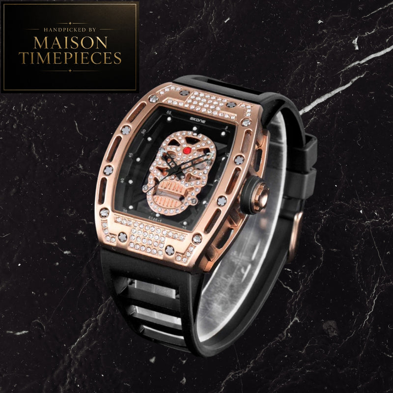 A luxury skeleton wristwatch with a rose gold case, crystal-embellished bezel, and a detailed skull dial, paired with a black strap. The watch is displayed on a black marble background next to a 'Handcrafted by Maison Timepieces' logo badge.