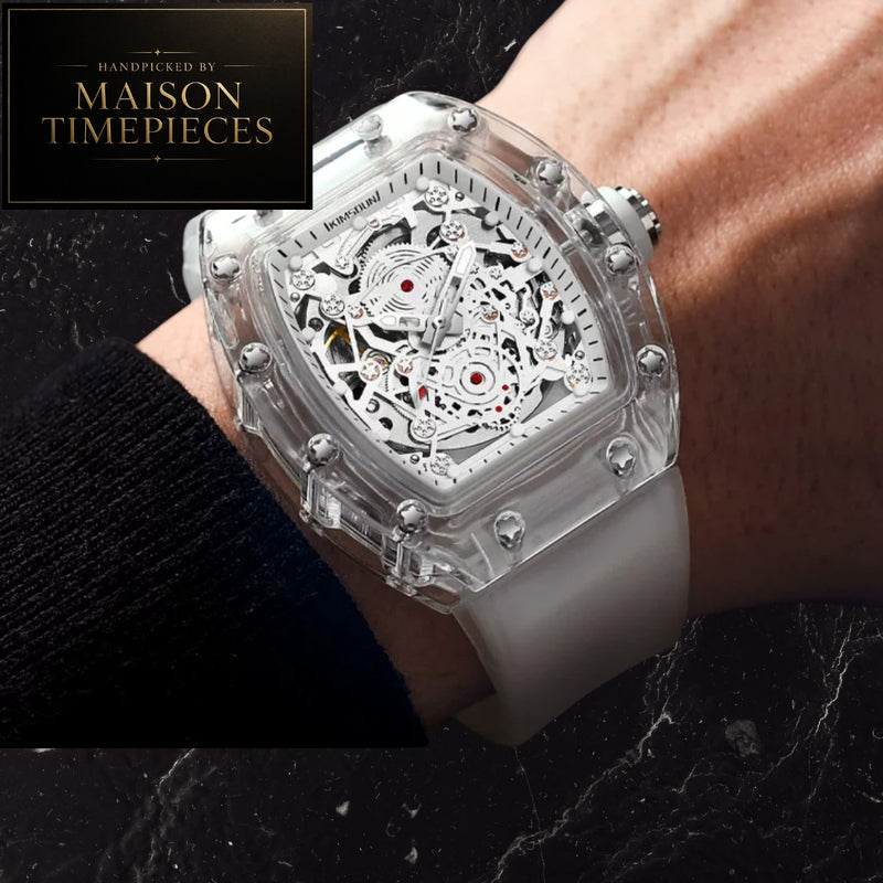 A Maison Timepieces skeleton watch with a transparent case and white silicone strap, shown worn on a wrist. The watch features a detailed silver-tone skeleton dial with red accents.