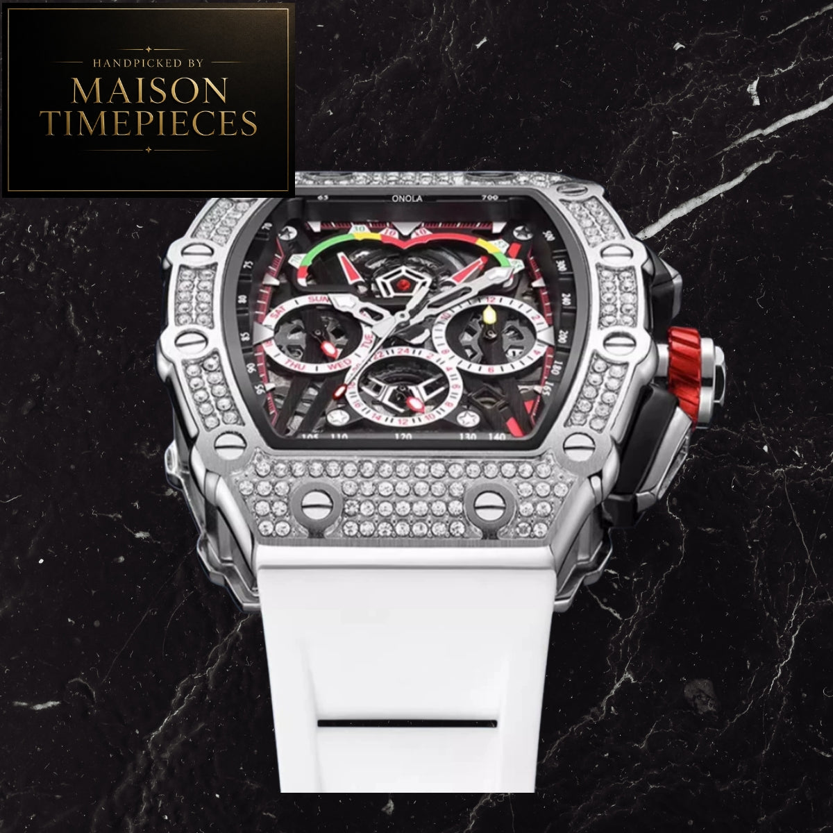 A luxury chronograph watch with a silver-toned case encrusted with diamonds, a black dial with red and green accents, and a white rubber strap, displayed on a black marble background with a Maison Timepieces logo in the top-left corner.