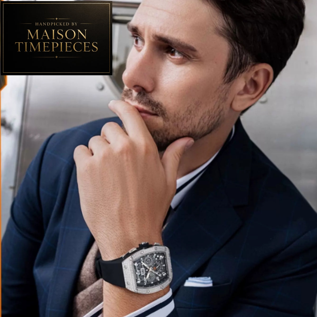 A man in a navy suit wearing a Maison Timepieces watch, with a logo overlay in the top-left corner.
