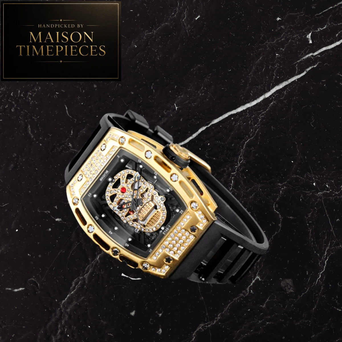 A luxury skeleton watch with a gold-tone case, diamond accents, and a black rubber strap, displayed diagonally on a black marble background. A logo overlay in the top-left corner reads 'Handcrafted by Maison Timepieces'.