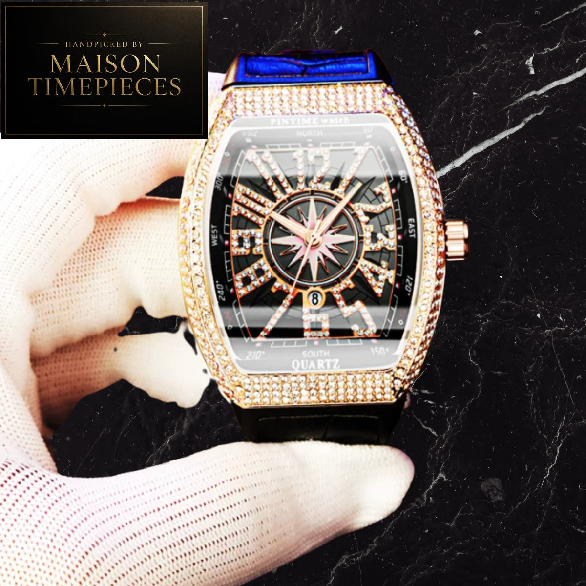 A luxury-style rectangular watch with a gold-tone rhinestone-encrusted bezel, black dial, and blue strap, held by a white-gloved hand against a black marble background. A Maison Timepieces logo appears in the top-left corner.