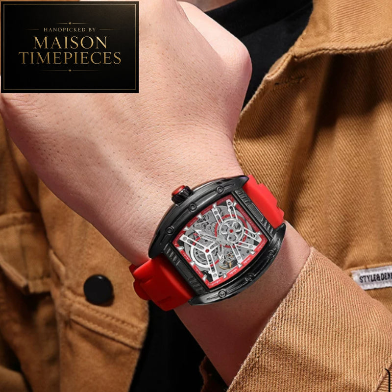 A close-up of a wrist wearing a Maison Timepieces skeleton watch with a black case, red strap, and silver inner dial, shown against a tan jacket background.