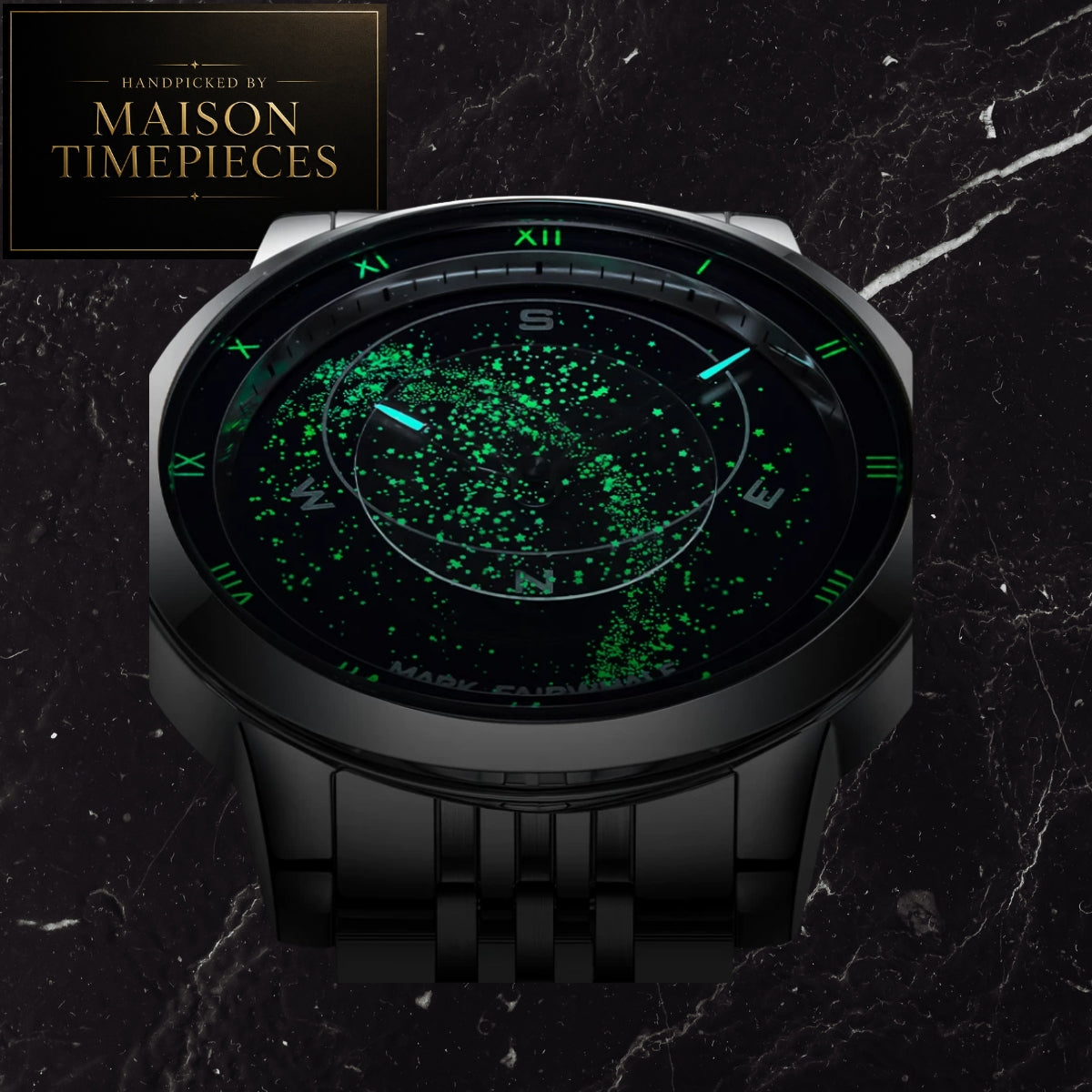 A Maison Timepieces round analog watch with a black metal case and integrated bracelet, featuring a glowing green galaxy-style dial with Roman numeral hour markers and blue-tinted hands, set against a dark marble background.