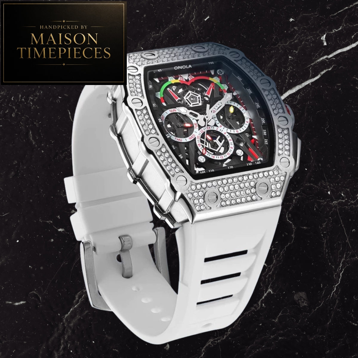 A luxury watch with a white silicone strap, a silver-tone bezel encrusted with rhinestones, and a black dial with multicolor chronograph subdials. The watch is displayed on a black marble background with a 'MAISON TIMEPIECES' logo in the top-left corner.