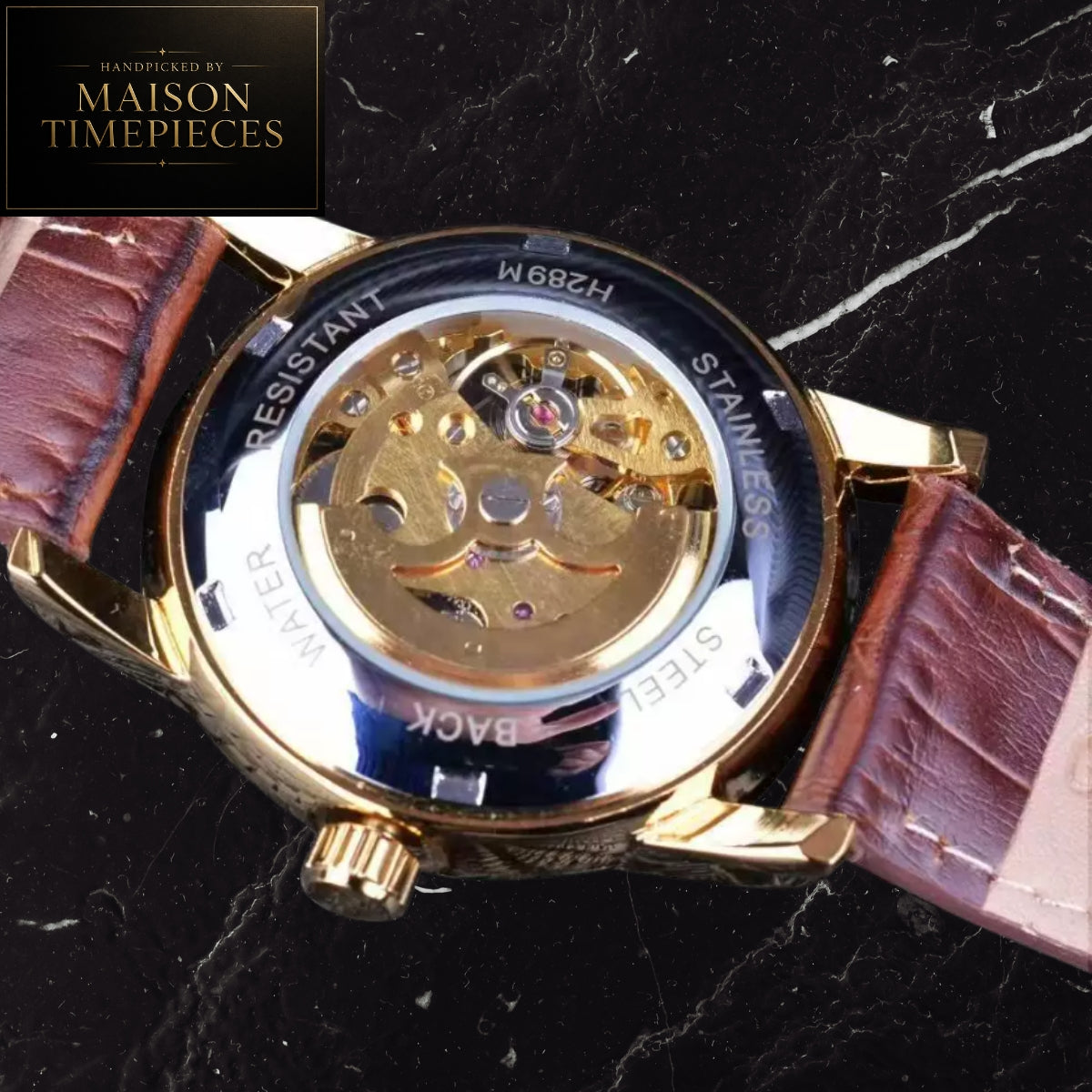 Close-up of the back of a wristwatch with a transparent case cover showing the gold-tone mechanical movement, on a dark marble surface. Brown leather strap ends are visible on both sides.