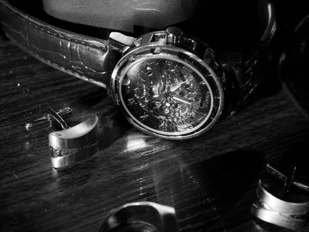 Close-up of a luxury mechanical wristwatch with a leather strap, surrounded by cufflinks and accessories on a polished dark wooden surface — symbolizing sophistication, craftsmanship, and timeless men's style.