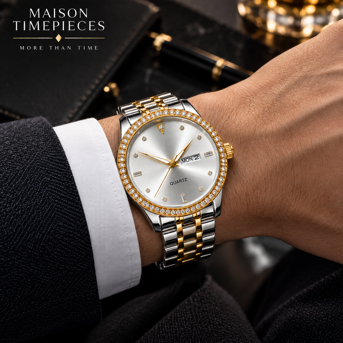 A close-up lifestyle shot of a men's two-tone stainless steel and gold watch with a diamond-encrusted bezel and white dial, worn on a wrist with a black suit jacket and white dress shirt cuff visible. The Maison Timepieces brand logo is in the top left corner.
